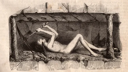 Ein junger Mann, der auf dem Boden liegt und die Decke eines Tunnels in einer englischen Kohlenmine aufpickt